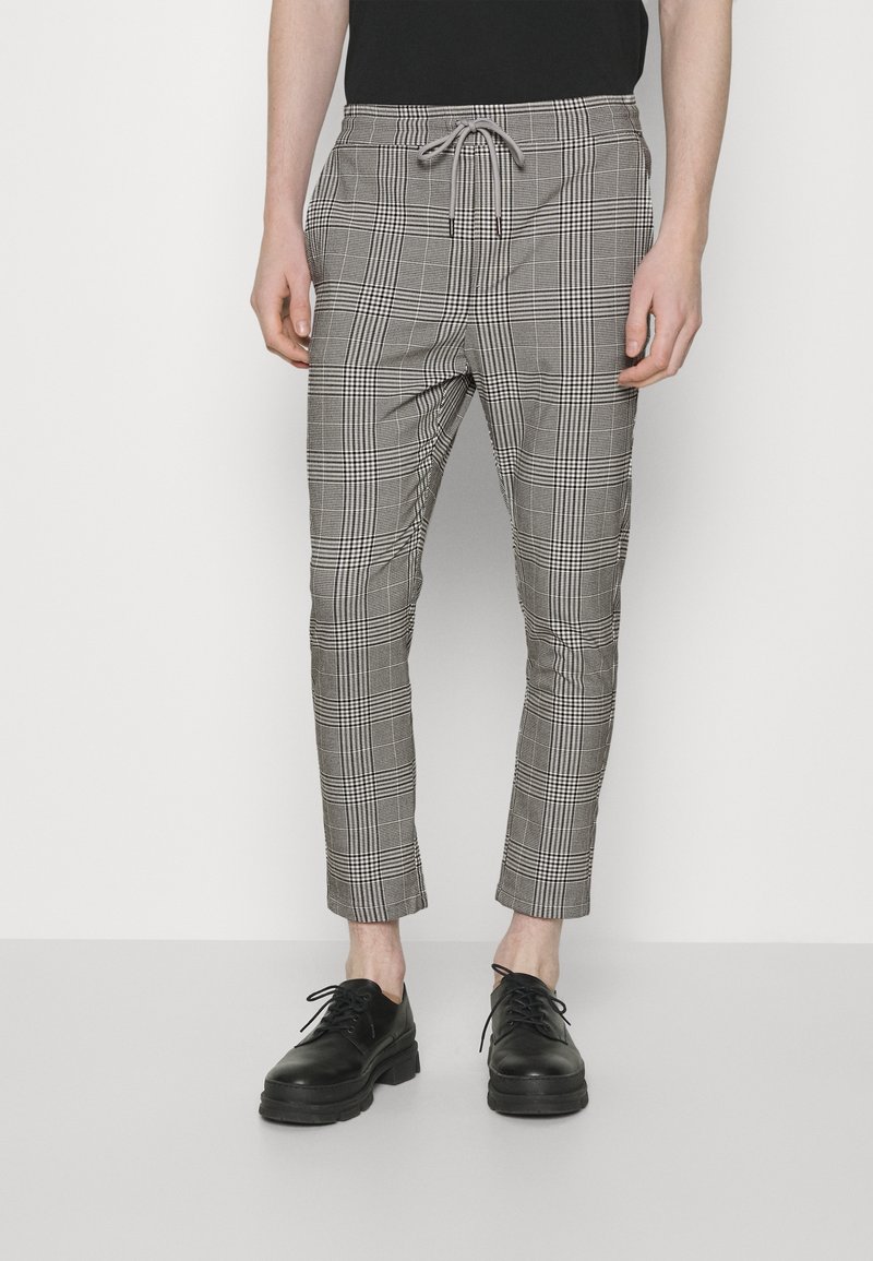 Geruit zwart-wit broek met een trekkoord in de taille, slim fit, taps toelopende pijpen en enkel lengte, gedragen met zwarte veterschoenen.