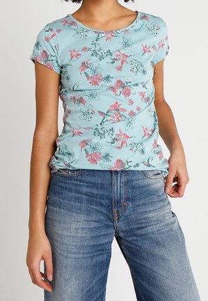 Top de manga corta de color azul claro con patrones florales en rosa y verde. Tela suave, diseño ajustado, cuello redondo, combinado con jeans de azul claro.