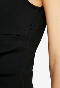 Svart åtsittande plagg med en slät textur, med en sidoglspp och sömdetaljer längs midjan som framhäver en strömlinjeformad siluett.