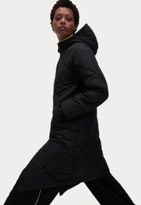 Cappotto lungo trapuntato nero con cappuccio, caratterizzato da un motivo diagonale, tasche laterali e una silhouette elegante e snella.