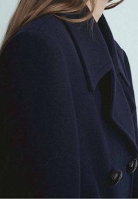 Merinovillasta valmistettu laivaston sininen takki, jossa on leveä kaulus, kaksirivinen malli ja mustat napit, esittää sileää ja teksturoitua pintamaa.