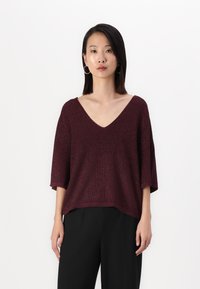 Bordeaux kort mouwen brei-top met een V-hals, beschikt over een losse pasvorm en een gestructureerde stof. Gecombineerd met zwarte broek met wijde pijpen.