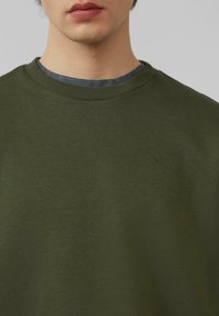 Oliwkowa bluza z okrągłym dekoltem wykonana z teksturowanej dzianiny; posiada subtelnie wyszyte logo na piersi oraz ribbowany dekolt.