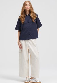 Navy button-up shirt with short sleeves, paired with loose white cargo pants and silver sneakers. Simple, modern design with clean lines.