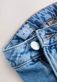 Jasnoniebieskie dżinsy z denimu o wyblakłym wykończeniu. Posiadają srebrne okucia, zapięcie na guzik i zamek oraz kontrastowe przeszycia wzdłuż szwów.