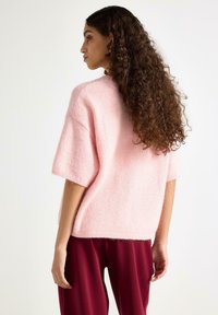 Lyserød, kortærmet sweater med blød tekstur og afslappet pasform, kombineret med bordeaux bukser. Ingen bemærkelsesværdige mønstre eller hardware synligt.