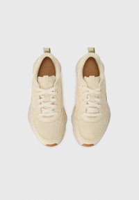 Kremfargede sneakers med mesh-overdel, kontrasterende gummisåle og flate snører. Har en pull tab på hælen for enkel påkledning.