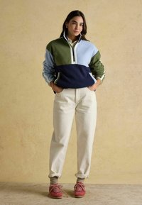 Fleeceová mikina v modrej, zelenej a námorníckej farbe s polovičným zipsom. V kombinácii s bielymi nohavicami s manžetami a ružovými teniskami pre neformálny vzhľad.