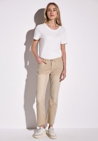 Beige chinos suora leikkauksella, joissa on etutaskut koristeompeleilla, yhdistettynä yksinkertaiseen valkoiseen T-paitaan ja vaaleisiin lenkkarityylisiin kenkiin.