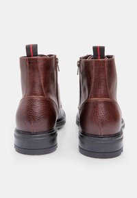 Stivaletti in pelle marrone con finitura texturizzata, dotati di suole nere e con linguette rosse sulla parte superiore. Chiusura con zip laterale.