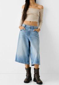 Beige stickad topp med off-shoulder och ljusblå vida jean culotter med framfickor, kombinerat med bruna ankelskor med metallaccenter.