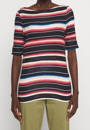 Person trägt ein kurzärmeliges Oberteil mit horizontalen roten, schwarzen, weißen und blauen Streifen und olivgrünen Hosen, gezeigt vom Hals bis zu den Hüften.