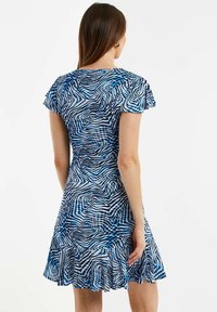 Vestido azul con estampado, con mangas cortas y acampanadas, un corsé ajustado y un dobladillo acampanado. Diseños abstractos de olas y cuadros en diferentes tonos de azul.