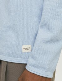 Pulover tricotat de culoare albastru deschis, cu țesătură texturată, guler rotund și manșete dintr-un material ribat. Are o etichetă cu inscripția "JACK & JONES" și "EST. 1990."