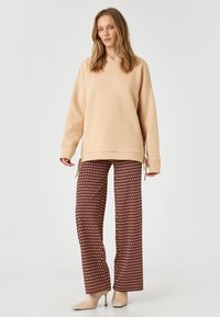 Beżowy, oversize hoodie ze sznurkiem u dołu, połączony z szerokimi spodniami w czerwono-kremowo-czarny wzór. Delikatna tekstura.