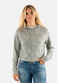 Haut en sweat gris à capuche zippé, présentant un motif en losanges matelassé et des perles décoratives. Manches longues et détails de cordon de serrage à la capuche.