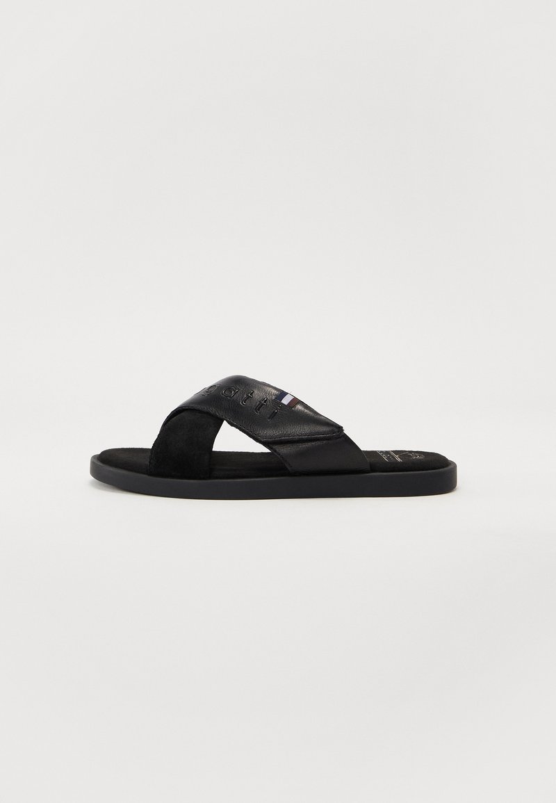 Svarte sandaler laget av lær og semsket skinn, med et kryss-design på stroppene og en flat gummisåle med preget logo og trikolor akcent.