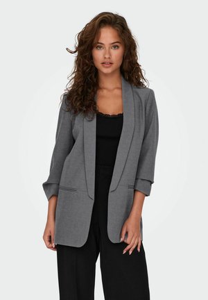 Grauer taillierter Blazer mit einem Schalkragen, Dreiviertelärmel und Fronttaschen. Getragen über einem schwarzen Oberteil und schwarzen Hosen.