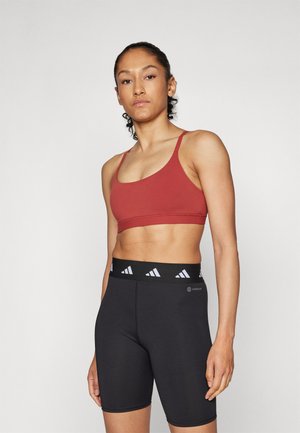Red athletic crop top with thin straps paired with black compression shorts featuring a branded waistband. Smooth fabric, fitted design.