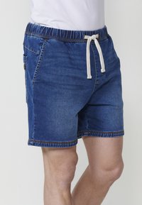 Džinsu šorti ar elastīgu jostu un baltu aukliņu, divām sānu kabatām un ziliem izšuvumiem. Gluda tekstūra un brīvs piegriezums.