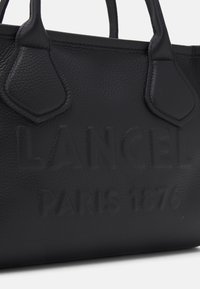 Czarna skórzana torebka z teksturowanym wykończeniem, z wytłoczonym logo "LANCEL PARIS 1876", mocnymi uchwytami i strukturalnym kształtem.