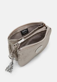 Beige Satin-Geldbörse mit einem Reißverschluss, ausgestattet mit einem Innenfach und einem Metall-Schlüsselanhänger in Form eines Bären. Markenlabel sichtbar im Inneren.
