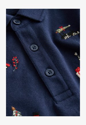 Tumman sininen viikonloppupaita, jossa on kolme mustaa nappia, ja sen pinnassa on värikästä brodeerausta, jossa on puita, lahjoja ja kukkaelementtejä.