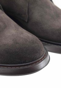 Stivali alla caviglia in suede marrone con punta arrotondata e suola in pelle liscia, che mostrano una superficie leggermente texture e un minimo dettaglio di cucitura.