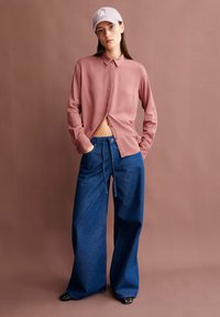 Light pink long-sleeve shirt with a button-down collar, paired with loose blue denim pants featuring a drawstring waistband and flat black shoes.