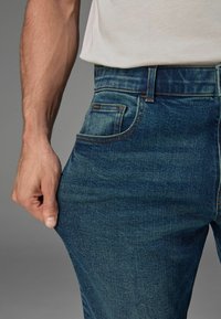 Jeans din denim albastru cu un design clasic cu cinci buzunare. Prezintă o croială dreaptă, decolorare subtilă și cusături în contrast de-a lungul cusăturilor.