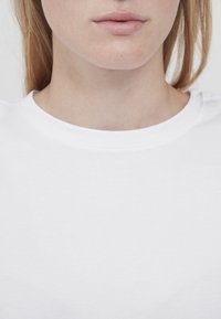 Hvid bomulds t-shirt med rund halsudskæring. Stoffet ser glat og udekoreret ud, hvilket viser et simpelt og rent design.