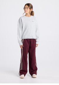 Sudadera gris de corte holgado, con un pequeño logotipo. Pantalones deportivos burdeos con franjas blancas laterales, silueta suelta y cintura elástica.