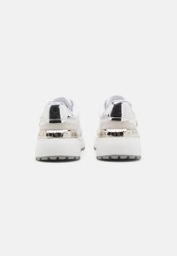 Fehér és szürke sneaker, texturált felső résszel, sima ezüst kiegészítőkkel és vastag fehér talppal. A logó látható a saroknál.