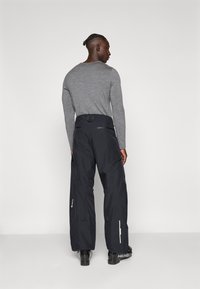 Zwarte waterdichte skibroek met een verstelbare tailleband, voorzien van een slank ontwerp en reflecterende accenten. Gelaagd stof en zijzakken.