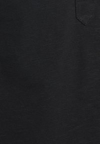 Tejido negro acanalado con patrón texturizado sutil y esquina de bolsillo cosida visible en la parte superior derecha.