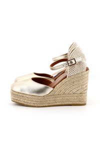 Scarpe espadrillas con zeppa in metallo dorato, cinturini in tessuto alla caviglia, punta rotonda, piattaforma in iuta intrecciata e dettaglio posteriore testurizzato.