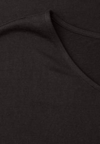 Nærbillede af foldet sort bomuldsstof, der viser strikket tekstur og overlappende kanter.