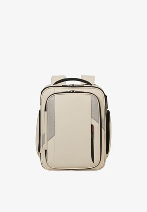 Beiger rechteckiger Rucksack mit schwarzen Reißverschlüssen, gepolsterten Trägern, Fronttasche mit Mesh-Details und einem oberen Tragegriff.