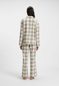 Beige, kräm, och brun rutigt pyjamas-set. Innehåller en knäppningstopp med långa ärmar och matchande utsvängda byxor. Tillverkat av mjukt tyg.