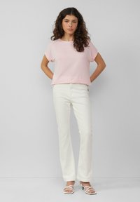 T-shirt rosa chiaro a maniche corte abbinato a jeans bianchi a palazzo, che mettono in evidenza una morbida texture del tessuto e una vestibilità rilassata. Semplici sandali bianchi con cinturino.