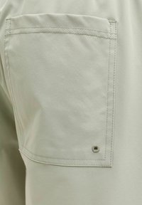 Φως μπεζ ύφασμα με τετράγωνη ραμμένη τσέπη με μικρό ενισχυμένο οφθαλμό κοντά στην κάτω γωνία.