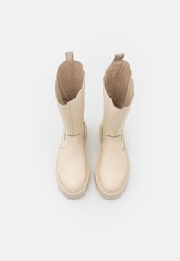 Botas de tobillo de cuero crema con textura suave, puntera redonda y detalles de costura. Presenta un suave forro interior y una tirador trasero.