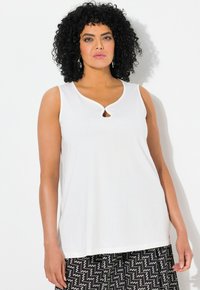 Bílý top bez rukávů s detaily ve tvaru klíčové díry na výstřihu. Vyroben z hladkého materiálu, má volný střih. Kombinovaný s vzorovanými kalhotami.