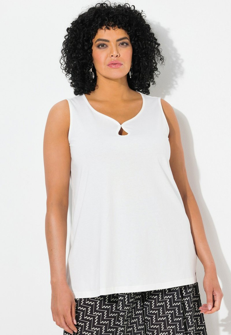 Bílý top bez rukávů s detaily ve tvaru klíčové díry na výstřihu. Vyroben z hladkého materiálu, má volný střih. Kombinovaný s vzorovanými kalhotami.