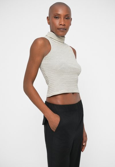 Top cropped de gola alta sem mangas, às riscas, em creme e preto, combinado com calças pretas de cintura elástica. Foco na textura e nas linhas horizontais.