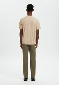 Chemise courte beige clair à manches courtes avec un col rond, en tissu à maille texturée et coupe décontractée, associée à un pantalon droit vert olive.