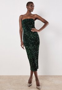 Grünes Pailletten-strapless Kleid mit einer figurbetonten Silhouette, knielangem Saum und Texture durch zahlreiche glitzernde Pailletten. Kombiniert mit nackten High Heels.
