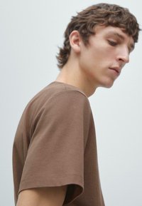 T-shirt marrone in cotone con scollo rotondo e maniche corte, caratterizzata da una trama liscia e un design semplice, senza motivi o grafiche visibili.