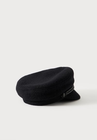Casquette plate en laine noire avec une courte visière et une bande tressée décorative au-dessus de la visière sur fond blanc.