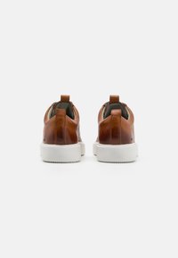 Brune lær-sneakers med hvite gummisåler, med en bakre trekkflik og glatt tekstur, som viser et minimalistisk design.